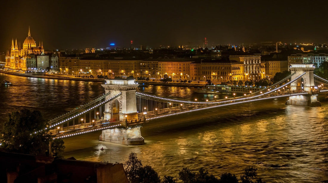 Night view of Budapest’s Chain Bridge and the Parliament building reflected in the Danube River, warm golden city lights creating a poetic and atmospheric scene.