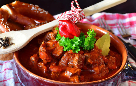 Traditional Hungarian goulash served in a rustic clay pot, with rich paprika sauce, fresh herbs and warm artisan table styling – an authentic Budapest food atmosphere.